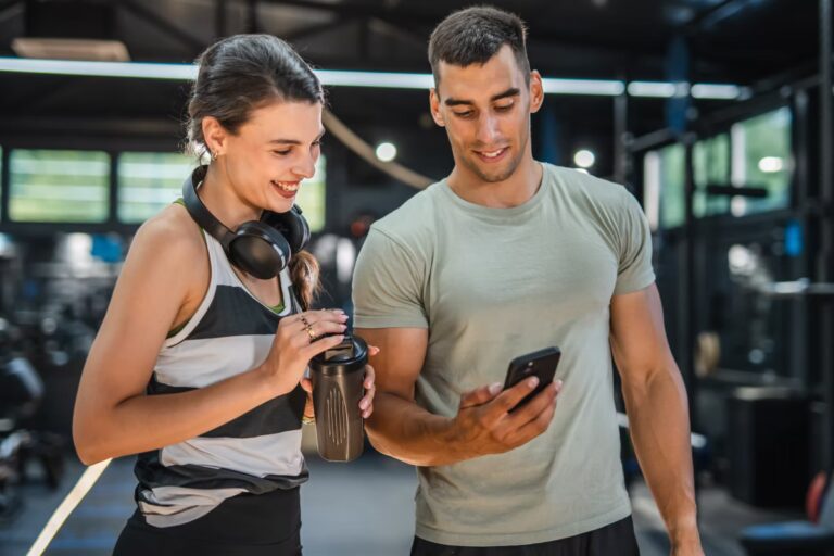 trener personalny z klientką na siłowni pokazuje coś na swoim smartfonie