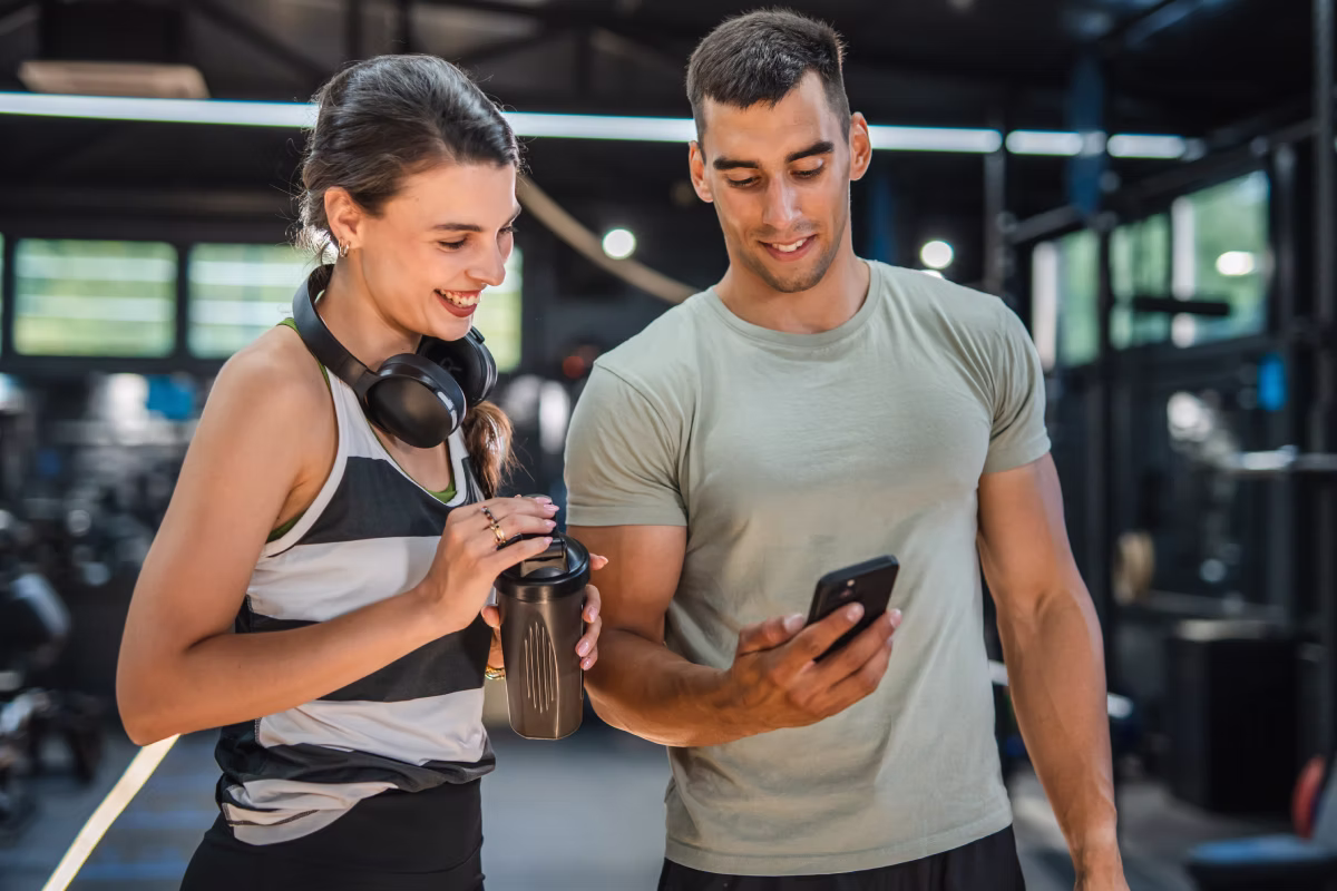 trener personalny z klientką na siłowni pokazuje coś na swoim smartfonie